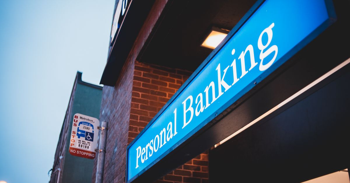 Fachada urbana de una entidad financiera con cartel y ventanales en una calle de barrio